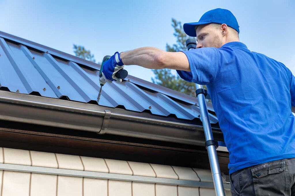 A roofer installing new shingles and insulation on a house with visible attic vents in early autumn.